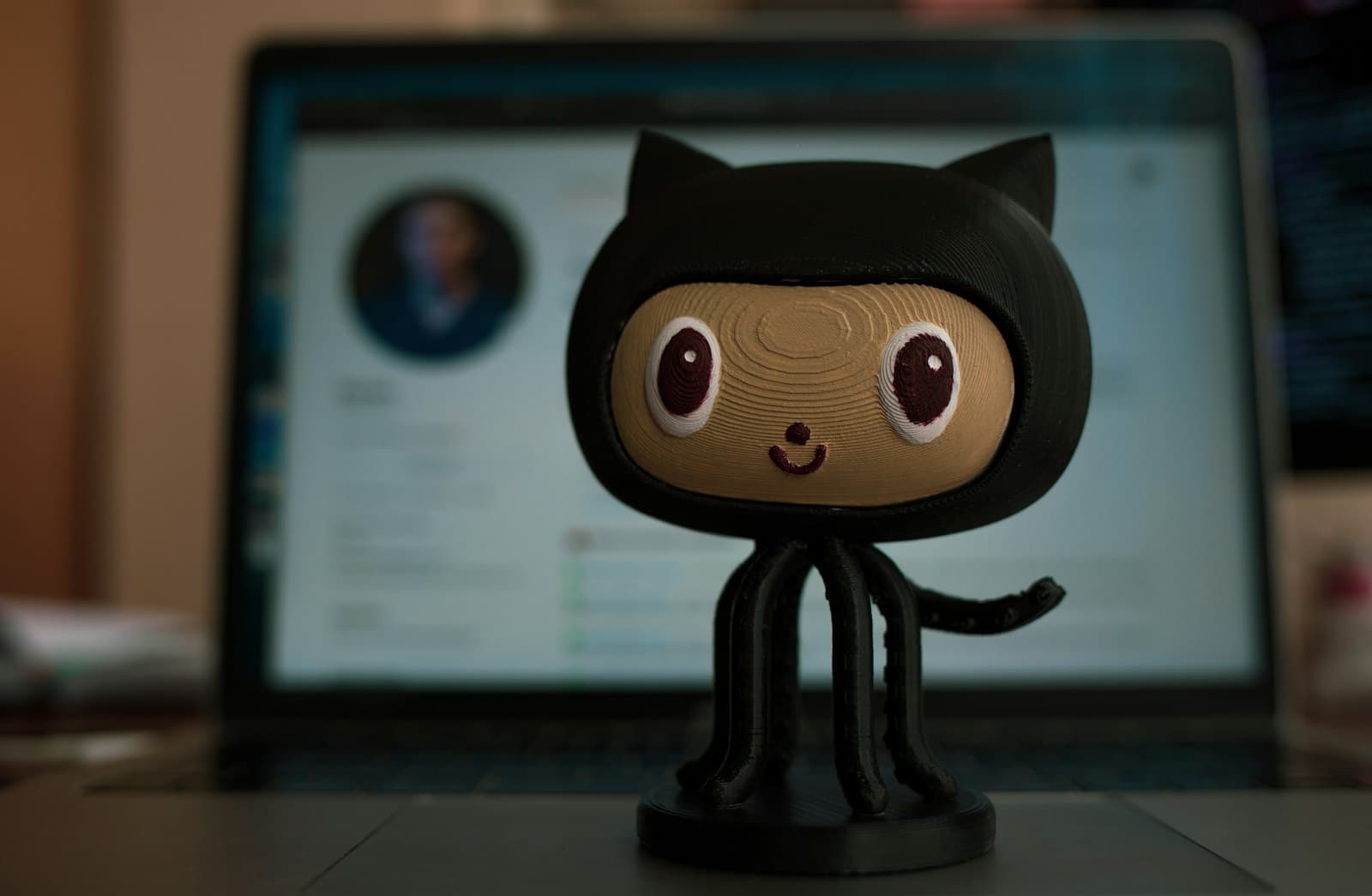 GitHub Octocat figurine on a laptop with a blurred profile on the display